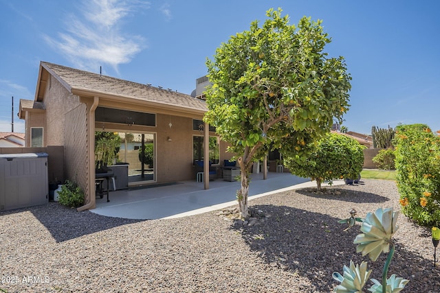 rear view of property featuring stucco siding, fence, roof with shingles, and a patio