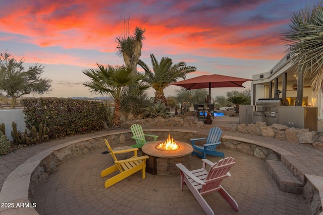 patio terrace at dusk featuring an outdoor kitchen and an outdoor fire pit