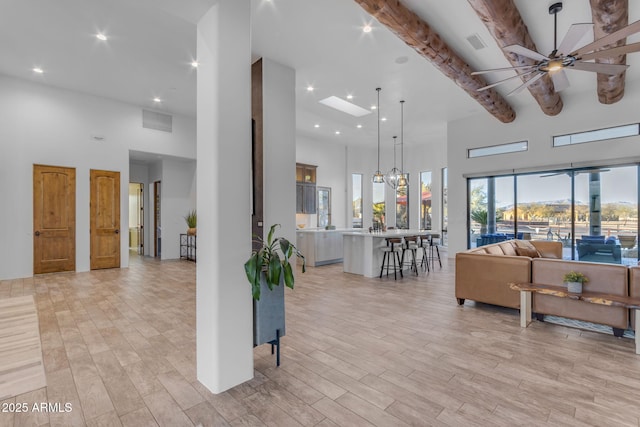 living room with a high ceiling, ceiling fan with notable chandelier, and light hardwood / wood-style floors