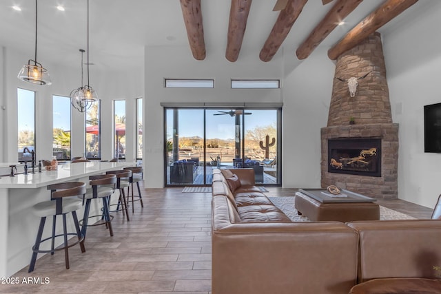 living room with a towering ceiling, a fireplace, beam ceiling, and light hardwood / wood-style flooring