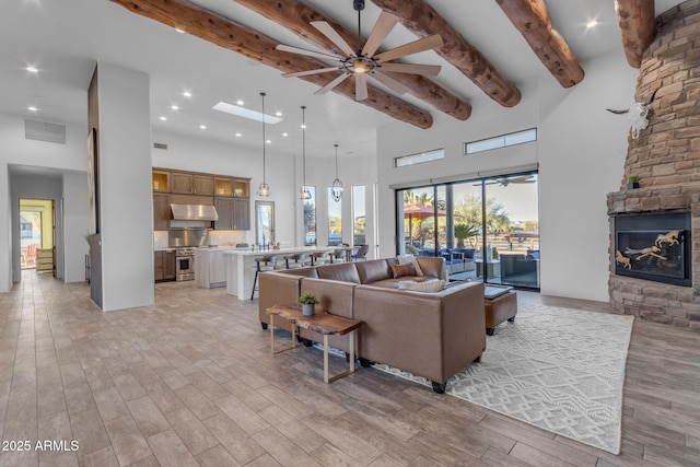 living room featuring ceiling fan, beam ceiling, a high ceiling, a fireplace, and light hardwood / wood-style floors