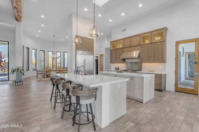 kitchen with a large island, extractor fan, hanging light fixtures, and built in refrigerator