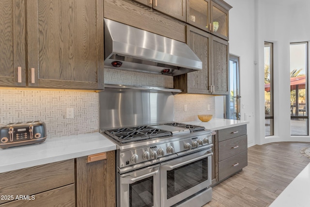 kitchen with decorative backsplash, ventilation hood, range with two ovens, and light wood-type flooring