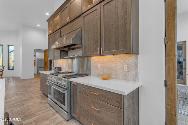 kitchen with double oven range, light hardwood / wood-style flooring, backsplash, and wall chimney exhaust hood