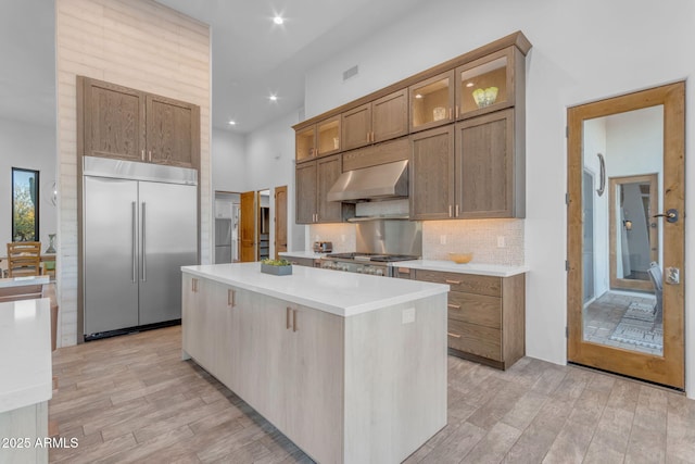 kitchen featuring backsplash, built in refrigerator, stove, a center island, and wall chimney exhaust hood