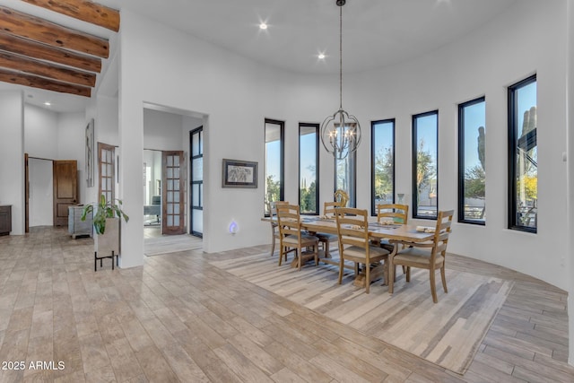 dining area featuring a towering ceiling, a notable chandelier, and light wood-type flooring