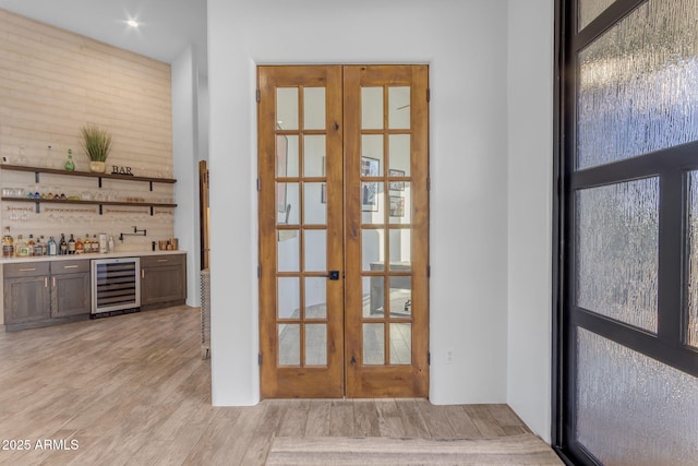 interior space with bar, wine cooler, light wood-type flooring, and french doors