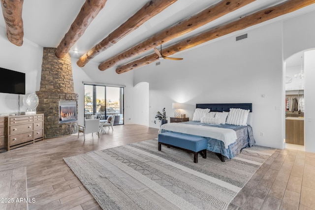 bedroom featuring a fireplace, a high ceiling, ceiling fan, beam ceiling, and light hardwood / wood-style flooring