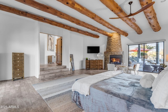 bedroom featuring beam ceiling, a stone fireplace, access to outside, and light hardwood / wood-style floors