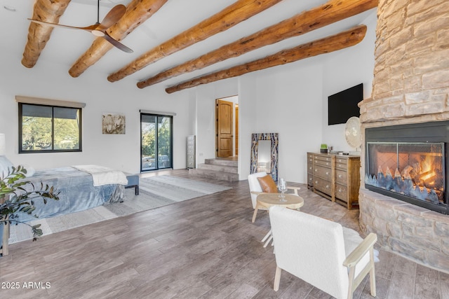 bedroom featuring hardwood / wood-style flooring, ceiling fan, a stone fireplace, and beam ceiling