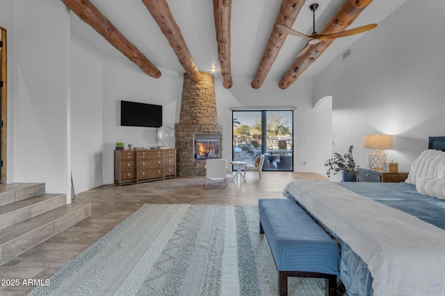 bedroom with beamed ceiling, wood-type flooring, a stone fireplace, and access to outside