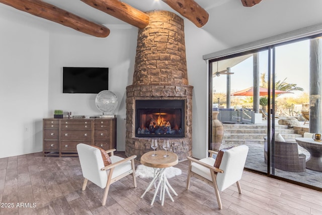 living room with a stone fireplace, hardwood / wood-style floors, and beam ceiling