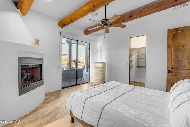 bedroom with a spacious closet, access to exterior, ceiling fan, beam ceiling, and light hardwood / wood-style flooring