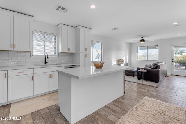 kitchen with a kitchen island, tasteful backsplash, white cabinetry, sink, and light wood-type flooring