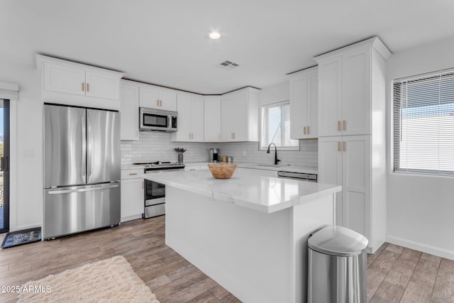 kitchen featuring sink, appliances with stainless steel finishes, white cabinetry, light stone counters, and a kitchen island