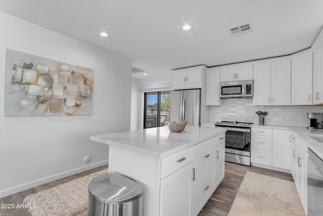 kitchen with a kitchen island, white cabinetry, decorative backsplash, light stone counters, and stainless steel appliances