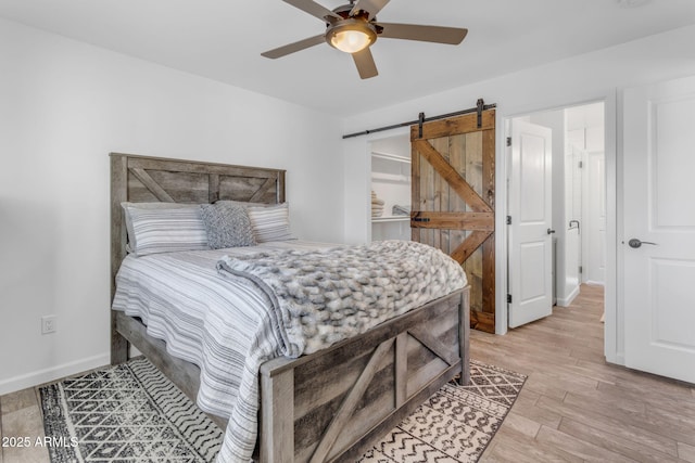 bedroom with ceiling fan, a barn door, and light hardwood / wood-style floors