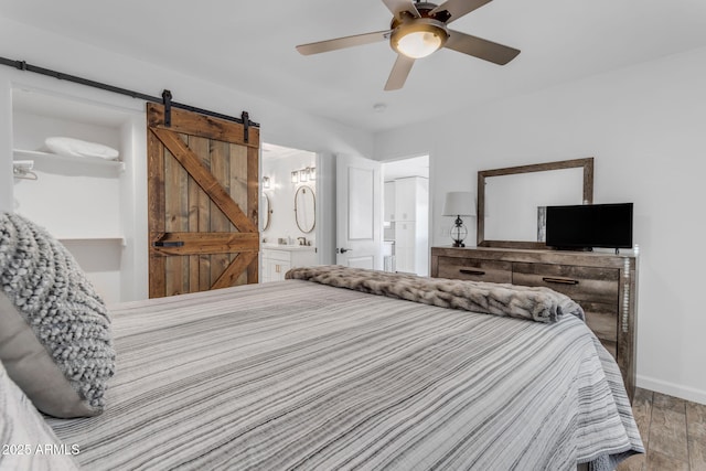 bedroom featuring light hardwood / wood-style floors, a barn door, ceiling fan, and ensuite bathroom