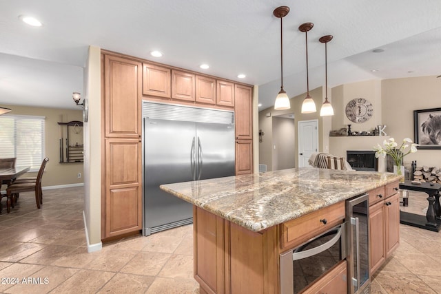 kitchen with light stone counters, hanging light fixtures, beverage cooler, and stainless steel built in refrigerator