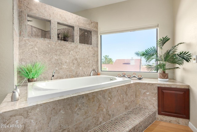 bathroom with a relaxing tiled tub and wood-type flooring