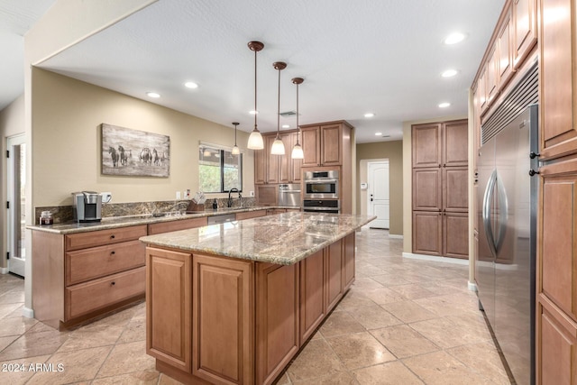 kitchen featuring light stone countertops, a center island, sink, hanging light fixtures, and stainless steel appliances