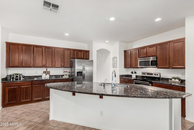 2986 E Country Shadows St, Gilbert, AZ 85298 - kitchen featuring appliances with stainless steel finishes, a sink, an island with sink, arched walkways, and dark stone counters