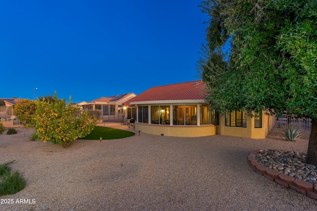 back house at dusk featuring solar panels, a patio, and a sunroom