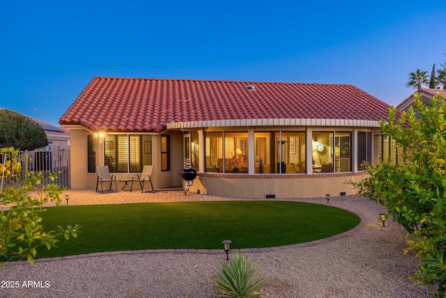 back house at dusk featuring a patio area and a yard