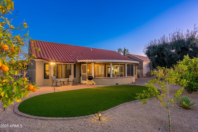 back house at dusk featuring a lawn and a patio