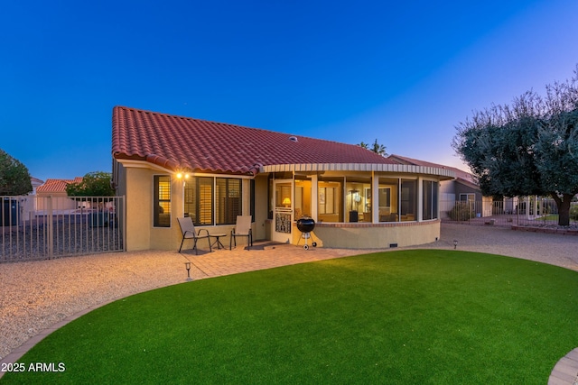 back house at dusk featuring a lawn and a patio