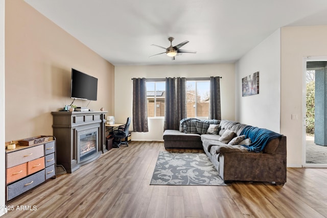 living area featuring plenty of natural light, wood finished floors, a glass covered fireplace, and a ceiling fan