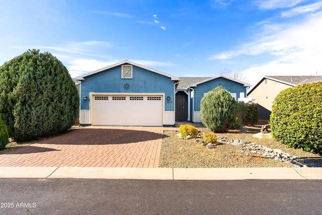 single story home featuring stucco siding, a garage, and decorative driveway