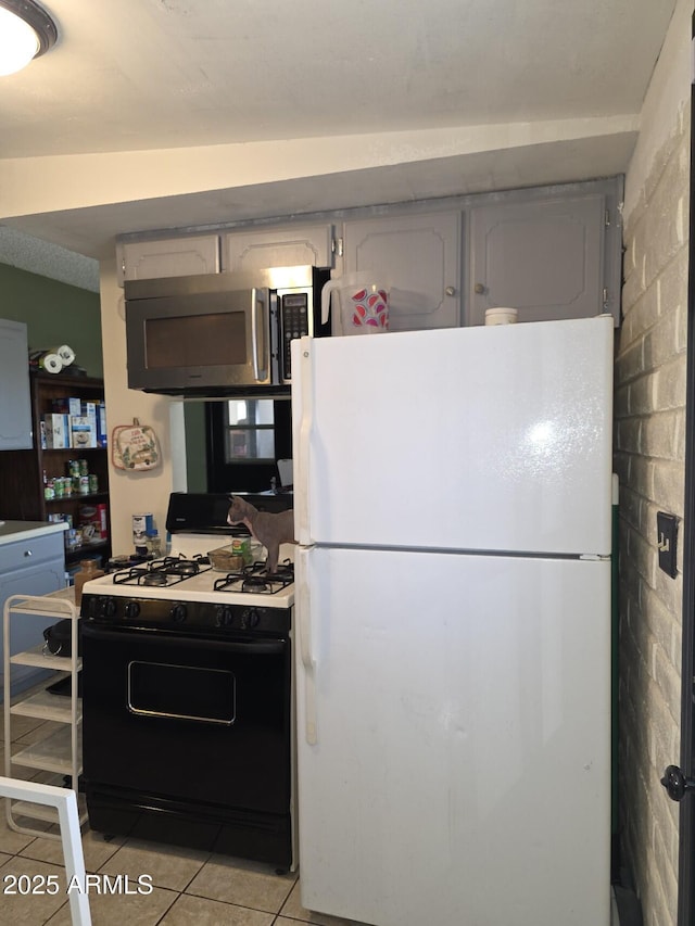 kitchen featuring gray cabinetry, stainless steel microwave, gas range oven, freestanding refrigerator, and light tile patterned floors