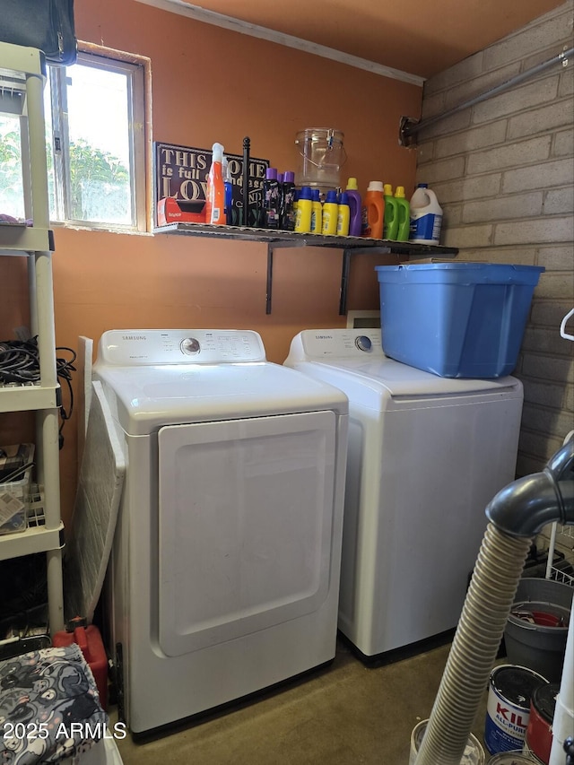 clothes washing area with laundry area, washer and dryer, and brick wall