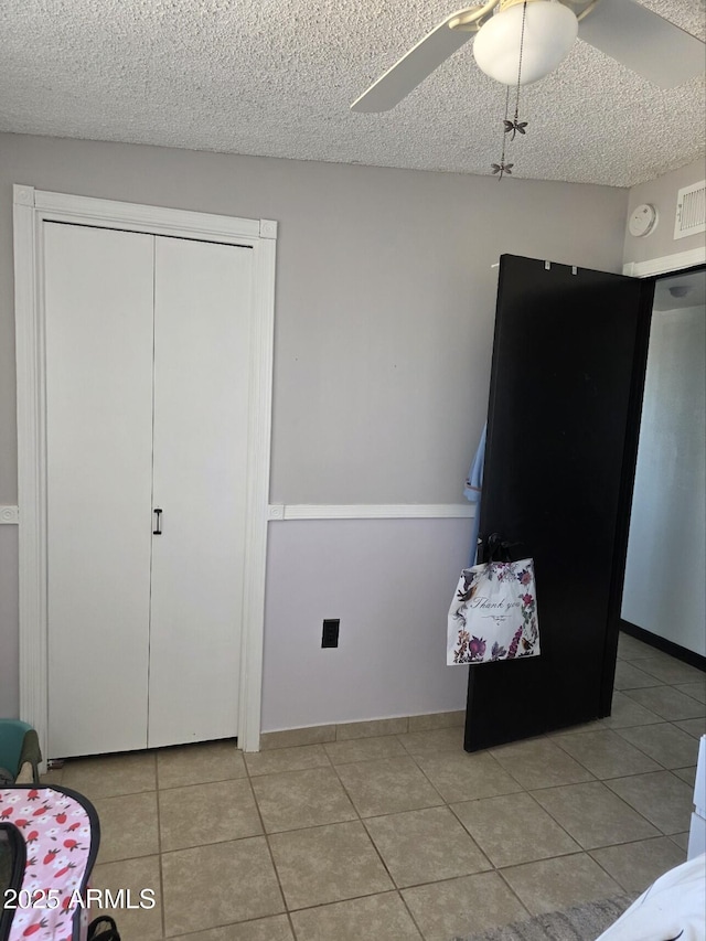 bedroom with light tile patterned floors, a ceiling fan, visible vents, a closet, and a textured ceiling