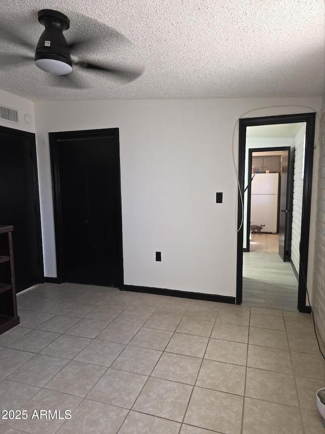 spare room with light tile patterned floors, visible vents, baseboards, and a textured ceiling