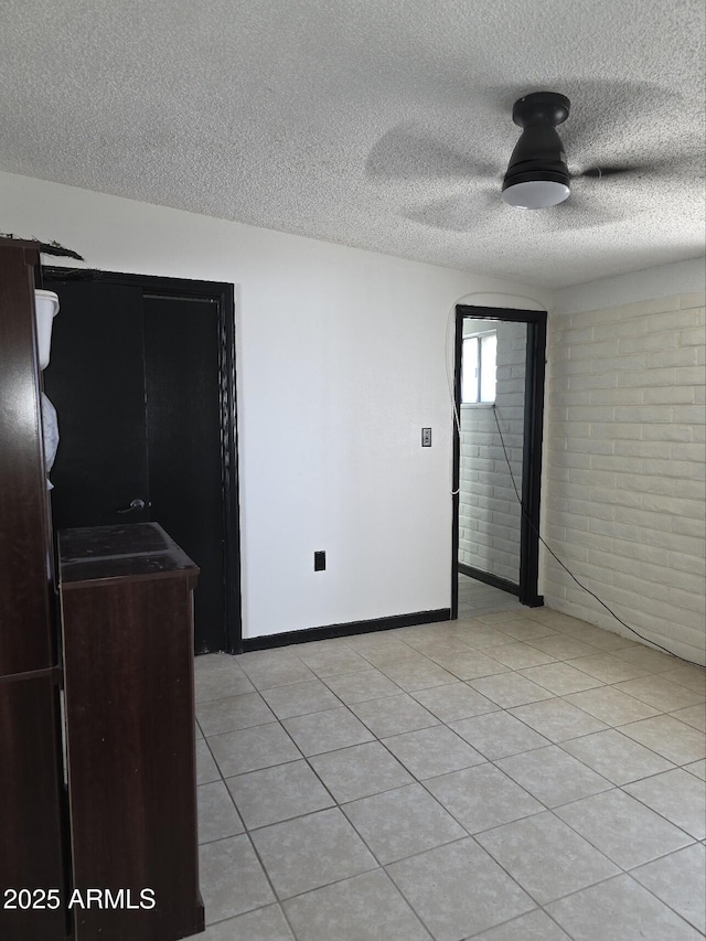 empty room with light tile patterned floors, baseboards, brick wall, and a textured ceiling