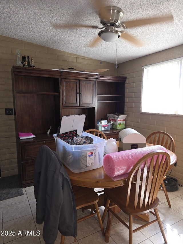 dining area featuring a textured ceiling, brick wall, light tile patterned flooring, and a ceiling fan