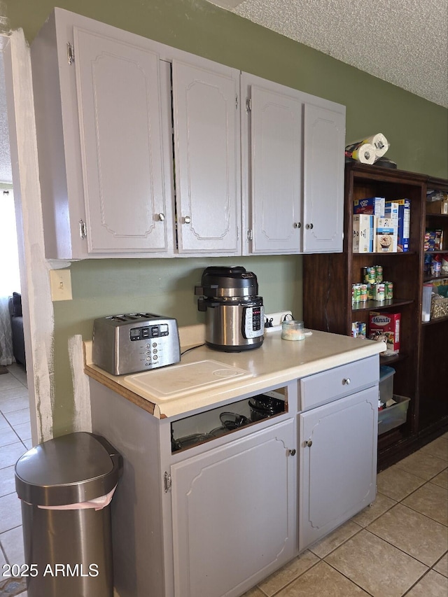 kitchen with light countertops, white cabinets, light tile patterned floors, and a textured ceiling