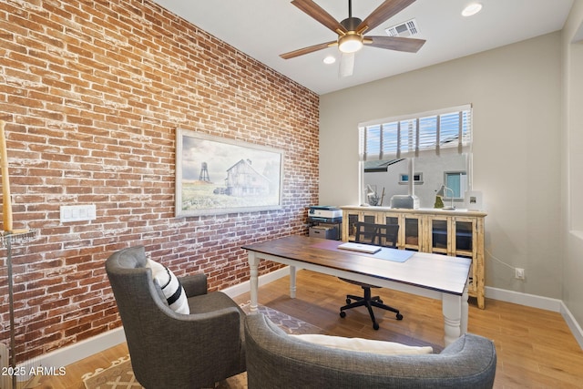 office area with light hardwood / wood-style floors, ceiling fan, and brick wall