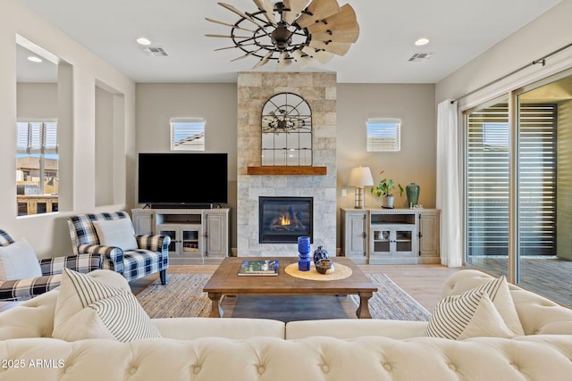 living room featuring a tile fireplace, ceiling fan, and light wood-type flooring