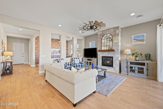 living room with light hardwood / wood-style flooring, a large fireplace, and ceiling fan