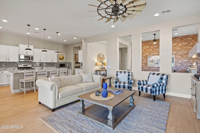 living room featuring light hardwood / wood-style flooring, ceiling fan, and brick wall