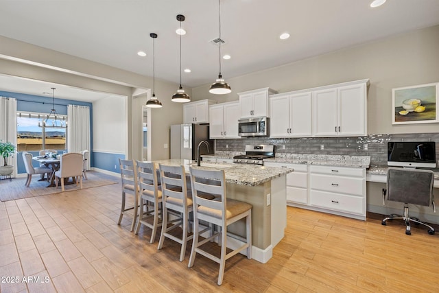 kitchen with white cabinetry, hanging light fixtures, stainless steel appliances, and an island with sink