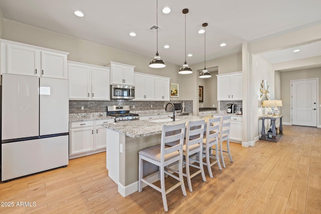 kitchen with a kitchen bar, white cabinetry, a center island with sink, appliances with stainless steel finishes, and pendant lighting