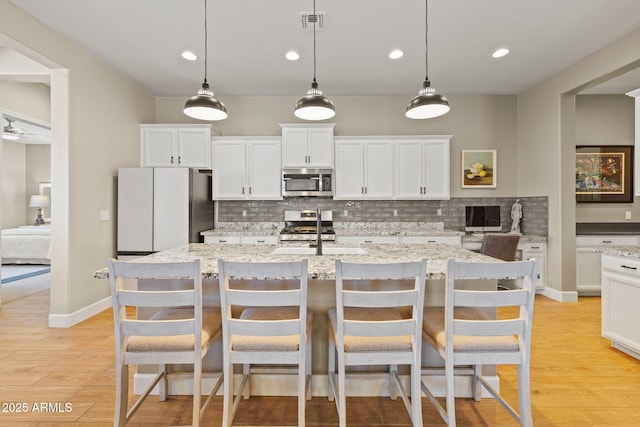 kitchen with a kitchen island with sink, decorative light fixtures, stainless steel appliances, and white cabinets