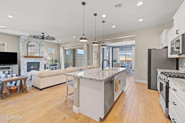 kitchen with sink, a center island with sink, pendant lighting, stainless steel appliances, and white cabinets