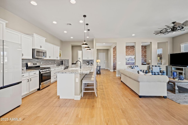 kitchen with white cabinetry, an island with sink, pendant lighting, stainless steel appliances, and light stone countertops