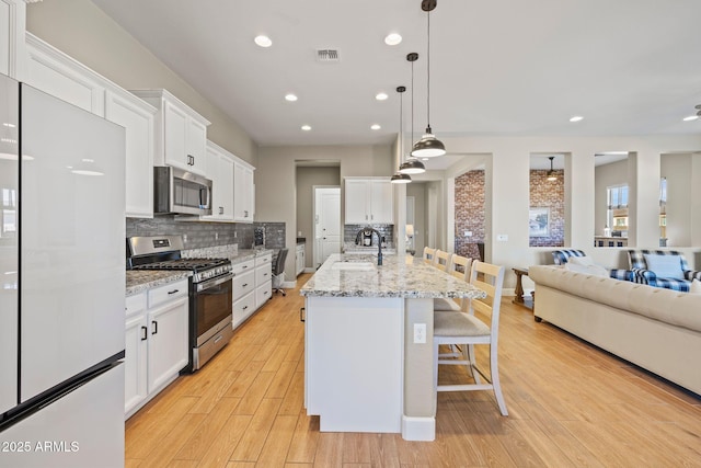 kitchen featuring pendant lighting, stainless steel appliances, a center island with sink, and white cabinets