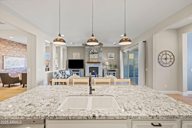 kitchen featuring pendant lighting, sink, light stone counters, a large fireplace, and white cabinets